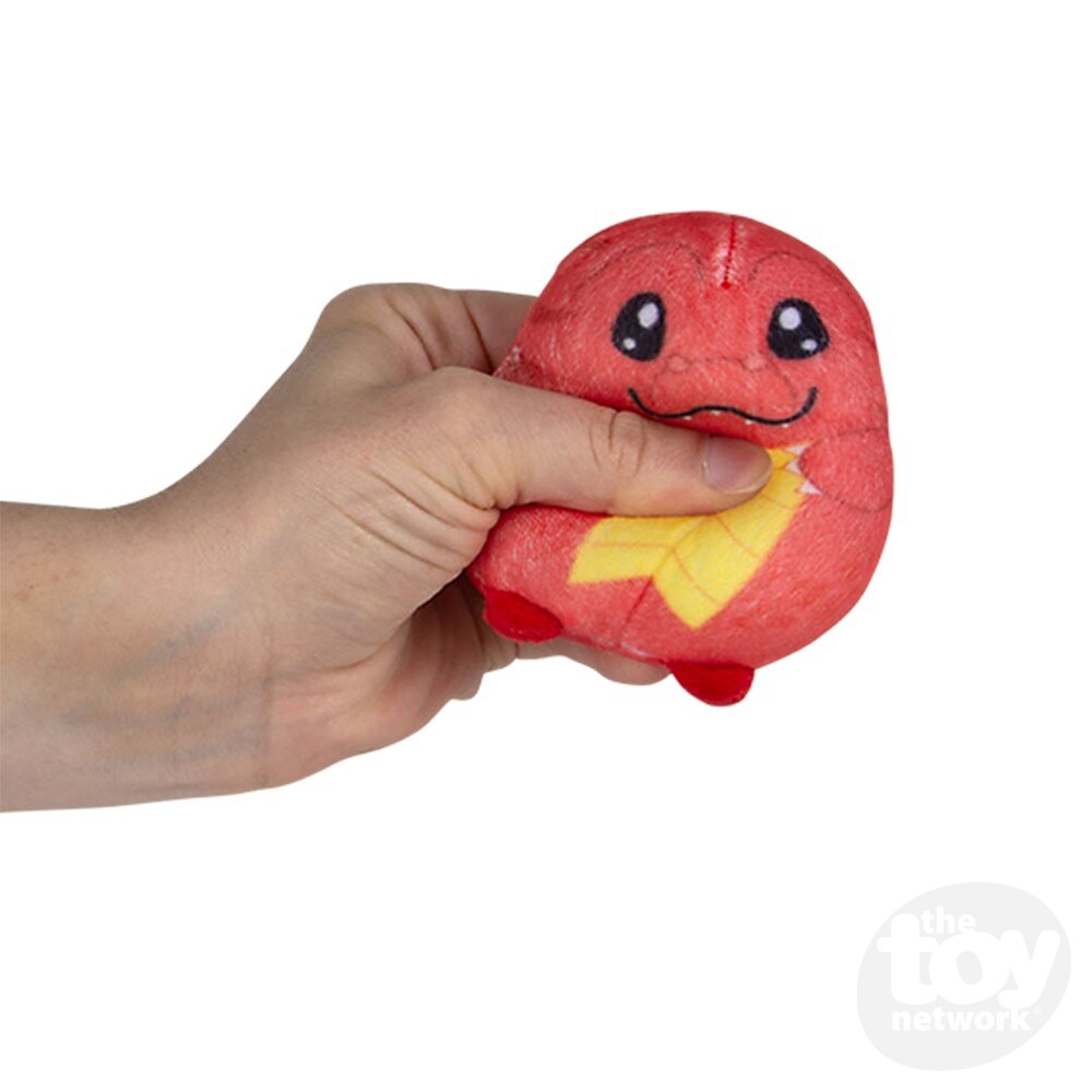 Hand squeezing a small plush toy shaped like a red creature with big eyes and a yellow pattern on its front—perfect for fidgety hands or as an eye-catching addition to any display box.