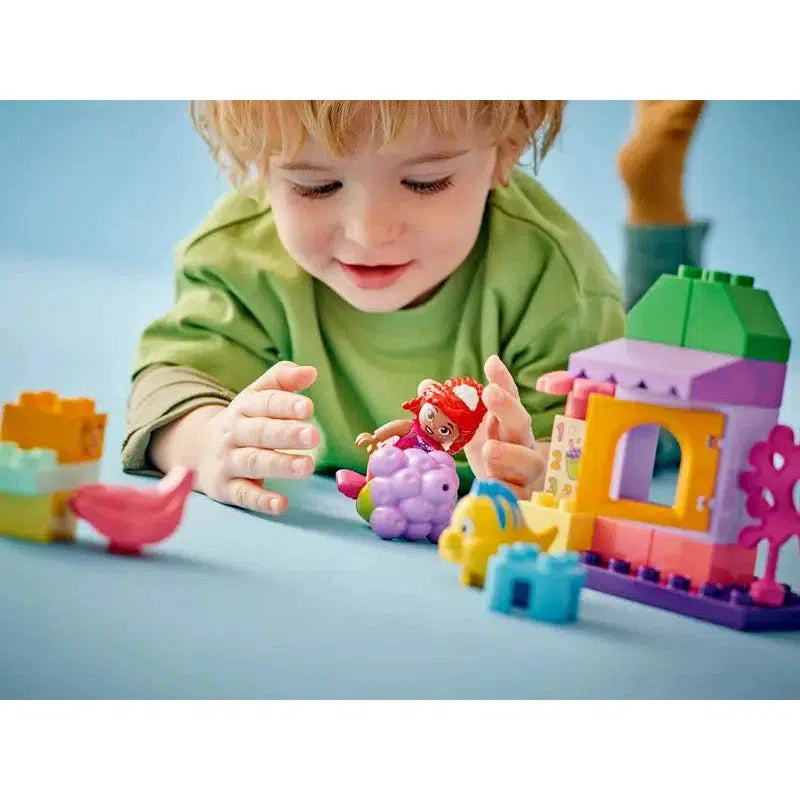 A child is joyfully playing with colorful building blocks and educational toys, including a figurine and a small house, on a light blue surface.