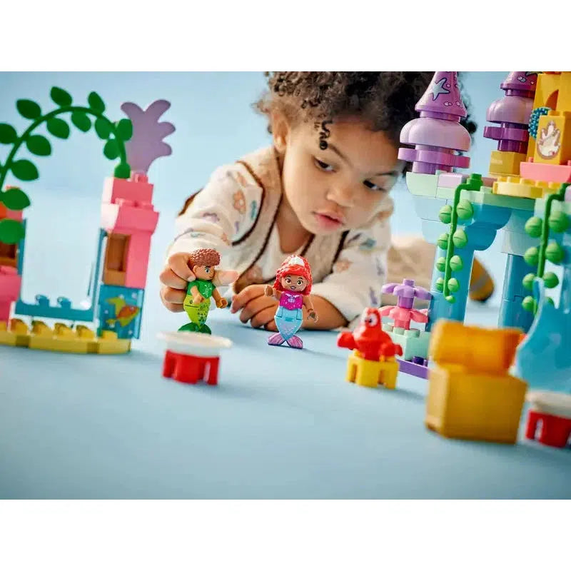 A toddler plays with colorful building blocks and toy figures on a light blue surface, creating an imaginative world inspired by LEGO DUPLO.