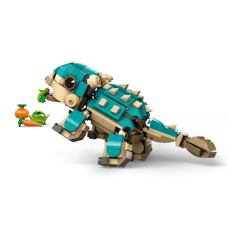 A teal and beige LEGO® armadillo-like creature, reminiscent of a Jurassic World dinosaur, holds a leafy branch in its mouth with carrots scattered nearby.