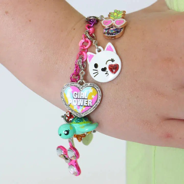 A wrist adorned with a vibrant charm bracelet showcasing a heart with "Girl Power," cat face, flowerpot, fidget spinner, and an enchanting sea turtle charm that adds a touch of ocean magic.