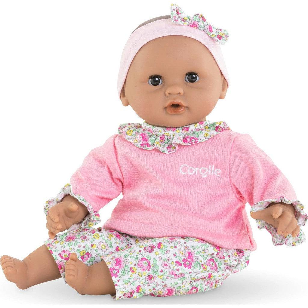 A doll dressed in a pink top and floral pants with a matching headband, sitting upright.