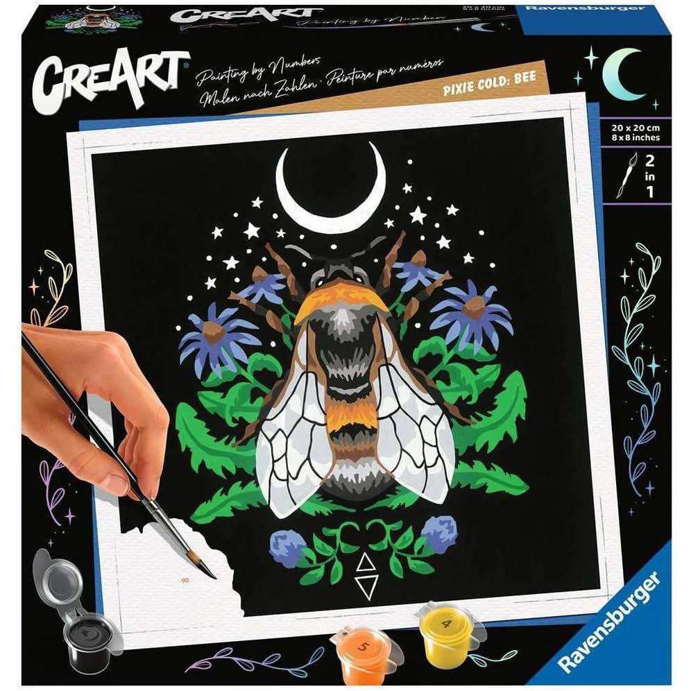 A person paints a colorful bee design on a square canvas with paint-by-numbers setup. The kit includes paints, a brush, and features a crescent moon and floral accents.