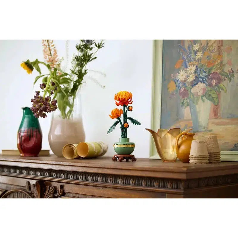 A wooden sideboard with vases of flowers, a potted plant, rolled papers, and ceramic items adds charm to your home office decor. A floral painting hangs on the wall above, complementing the display with a touch of artistry.