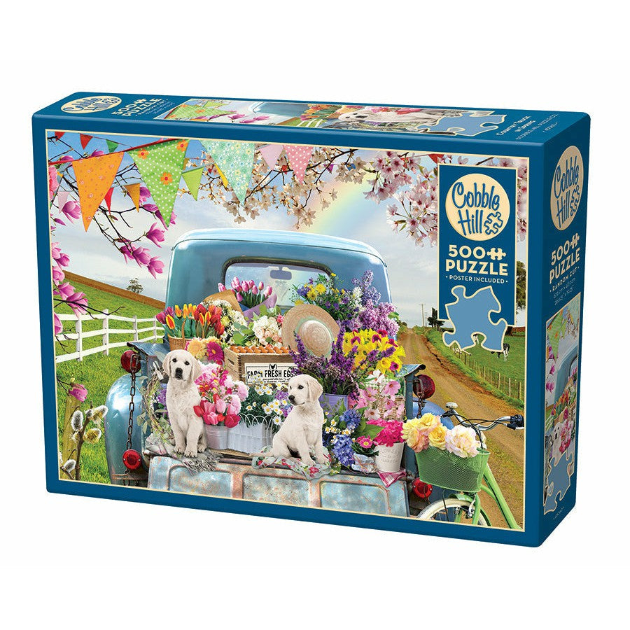 A 500-piece Cobble Hill puzzle featuring an old blue truck with flowers, puppies, and colorful decorations in a countryside scene.