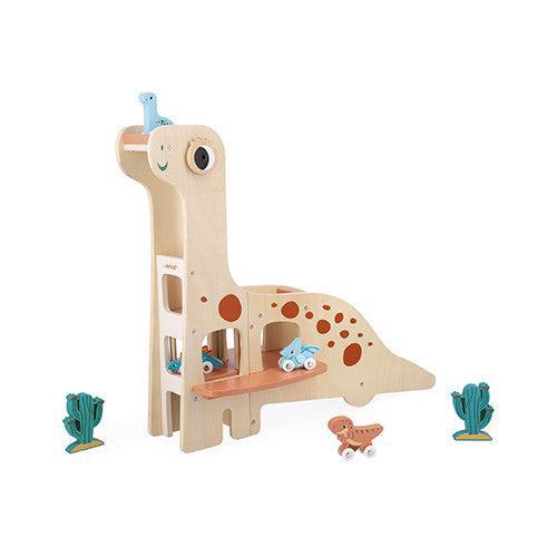 Wooden dinosaur-shaped toy ramp with small dinosaur and cactus figures placed around it. Several toy cars are positioned on the ramp and the ground.