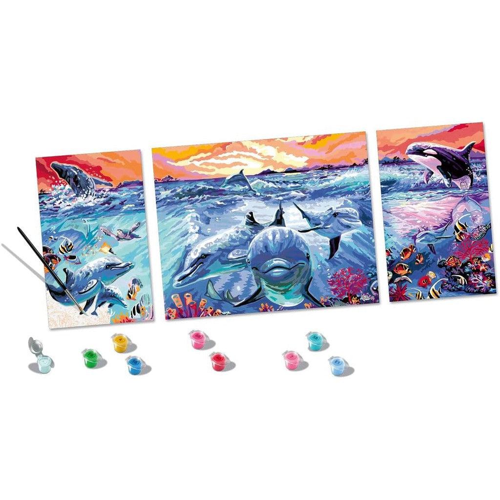 Experience the mesmerizing "Dolphins at Sunset" with this three-panel painting. Dive into an ocean scene of dolphins and fish, enhanced by colorful paint pots and a brush, reminiscent of a Ravensburger CreArt Paint by Numbers Kit waiting for your creative touch.