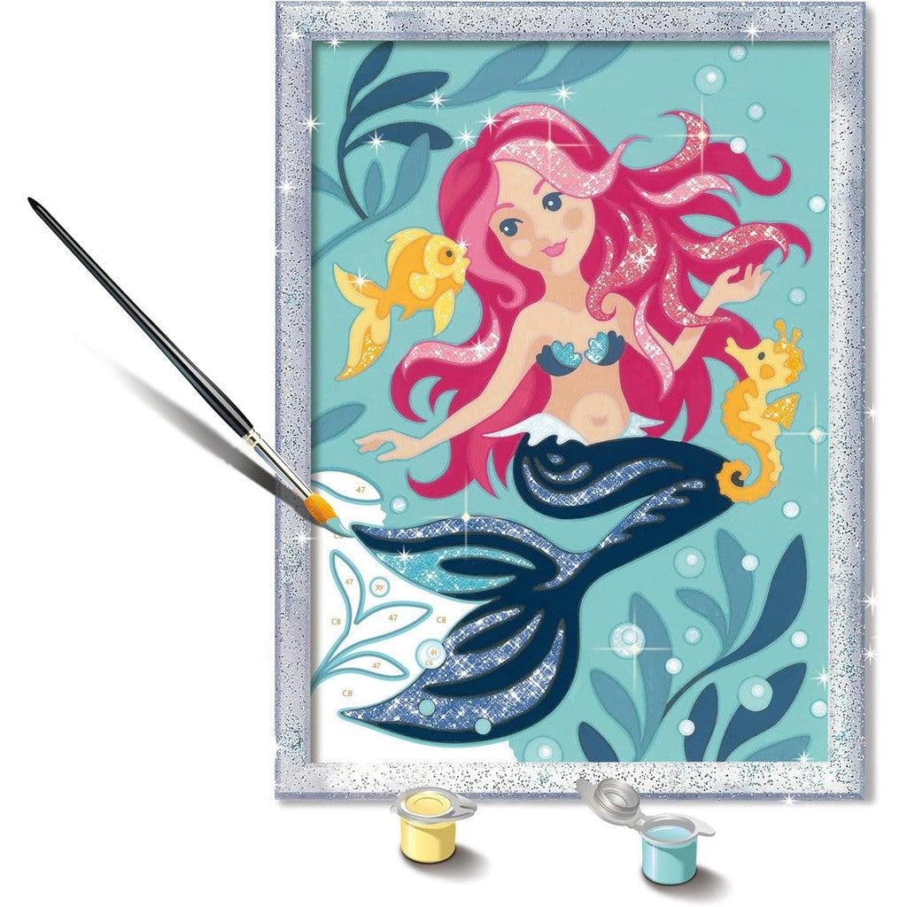 The Ravensburger Enchanting Mermaid Paint by Numbers Kit features a delightful scene with a pink-haired mermaid, a seahorse, and a fish. Included are a paintbrush and two vibrant paint pots in yellow and blue, perfect for immersing yourself in the joys of painting arts and crafts.