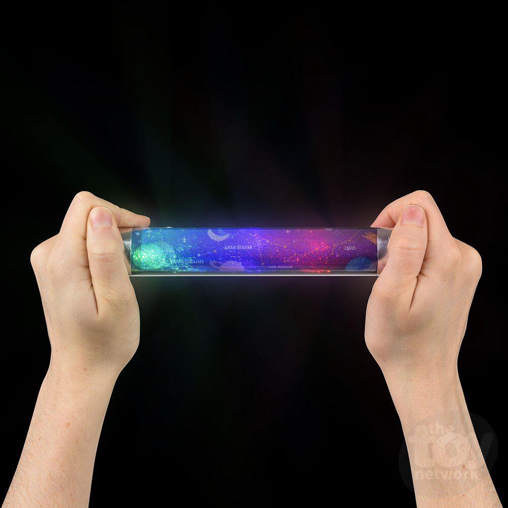 Hands holding a transparent Cosmic Energy Rod reveal a colorful, glowing galaxy pattern on a black background.