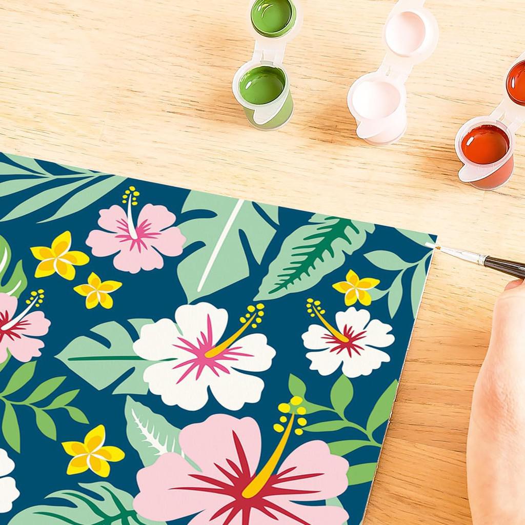 A person diligently paints a floral design with pink, white, and yellow flowers on a blue background, using the vibrant hues from their Ravensburger CreArt set. Nearby, paint pots in green, pink, and orange await their turn to bring the Painting Arts and Crafts project to life.