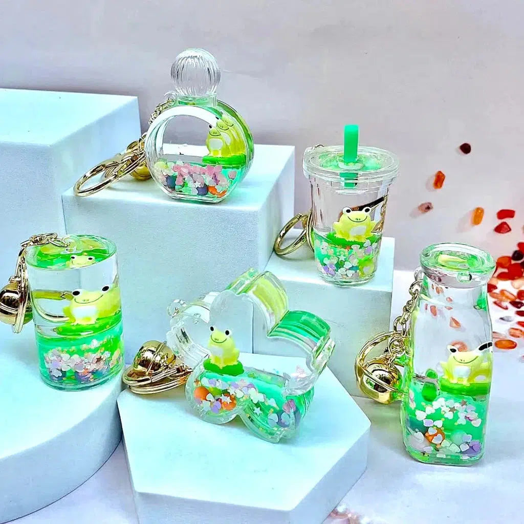 Five frog-themed key charms in various shapes, filled with green liquid and colorful beads, reminiscent of a silly animal or Frog Boba Floaty, displayed on hexagonal platforms.