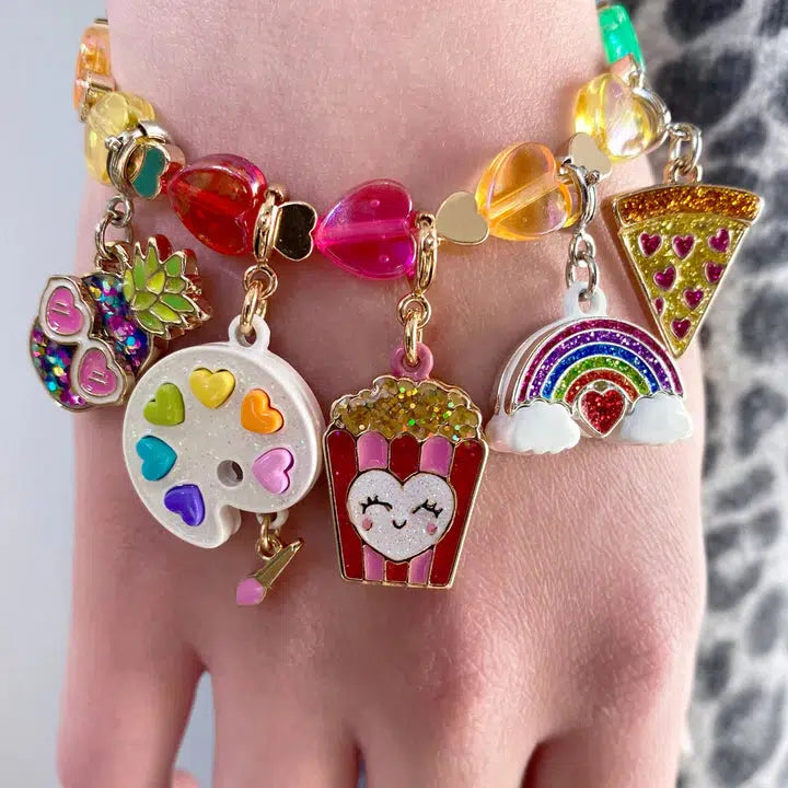 Close-up of a wrist adorned with a charm bracelet, featuring colorful trinkets like a pizza slice, glitter rainbow charm, popcorn, paint palette, and pineapple. Perfect for those looking to customize her collection with playful flair.