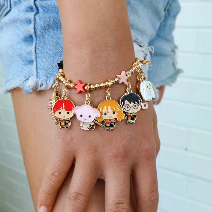 Close-up of a hand adorned with a stretch bead bracelet featuring cartoon character charms. The person, in blue denim shorts, stands against a white brick background, as if ready to step into the wizarding world.