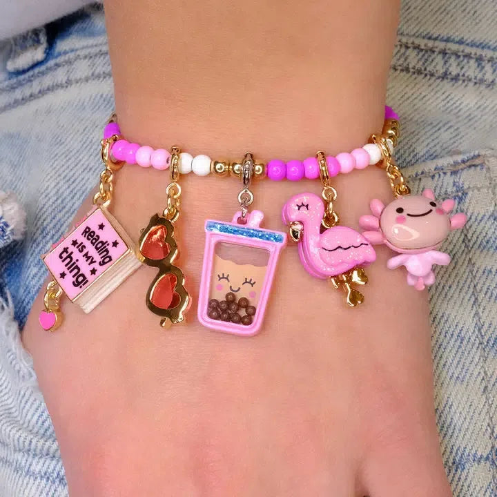 Worn on the wrist, this CHARM IT! bracelet features a delightful mix of colorful beads and charms, including a book, sunglasses, bubble tea, a flamingo, and a doll. A Gold Glitter Seal adds an extra touch of sparkle to this playful accessory.