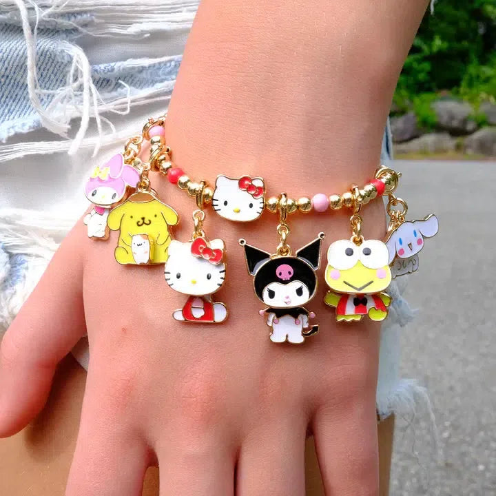 A close-up of a wrist adorned with a CHARM IT! bracelet featuring colorful Sanrio character charms, including Hello Kitty, My Melody, and Keroppi, complemented by whimsical Cinnamaroll charm details against a backdrop of frayed denim shorts.