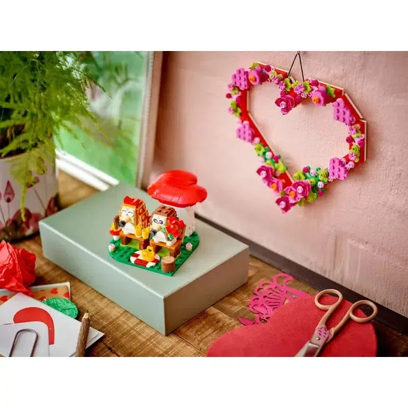 The lego set is shown on top of a box on a wooden desk next to a lego heart wall decoration (sold separately)