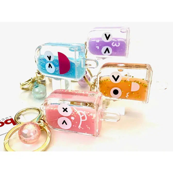 Four colorful keychains featuring silly animal cartoon faces are shown. Each is filled with liquid and small beads, attached to a gleaming gold key ring.