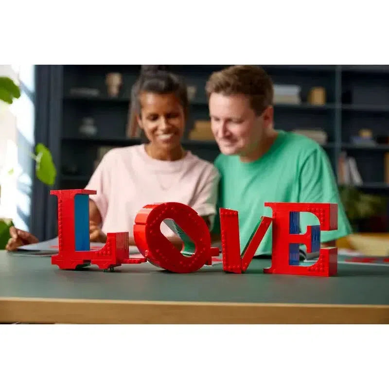 a couple sitting at a table blurred slightly behind the lego set almost finished sitting on the table