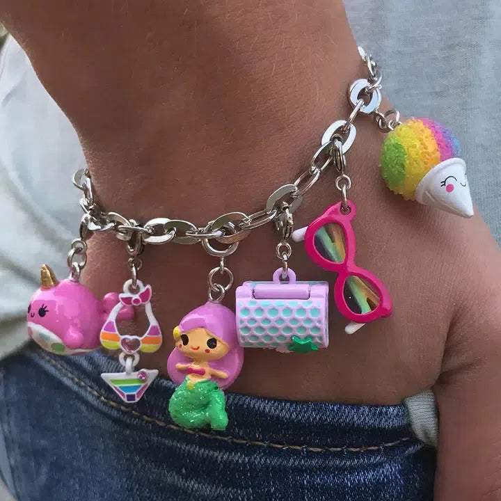 A charm bracelet graces the wrist, dazzling with its silver sheen. Perfect for any mermaid lover, it features enchanting charms—a unicorn, rainbow, pink sunglasses, handbag, ice cream cone—and the highlight: a mermaid reminiscent of sunken treasure dreams.