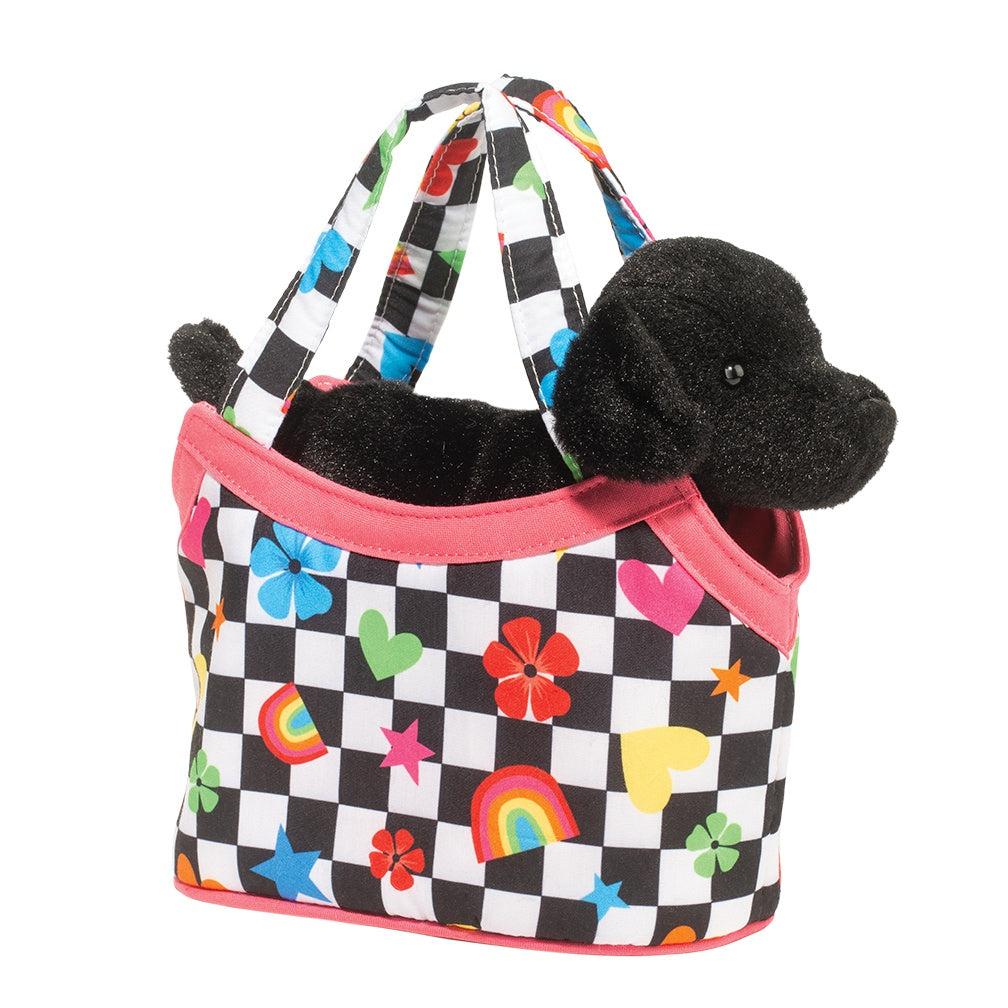 A black Labrador Retriever stuffed animal is cozily nestled inside a vibrant Sassy Pet Sak adorned with hearts, stars, flowers, and rainbows against a checkered backdrop.