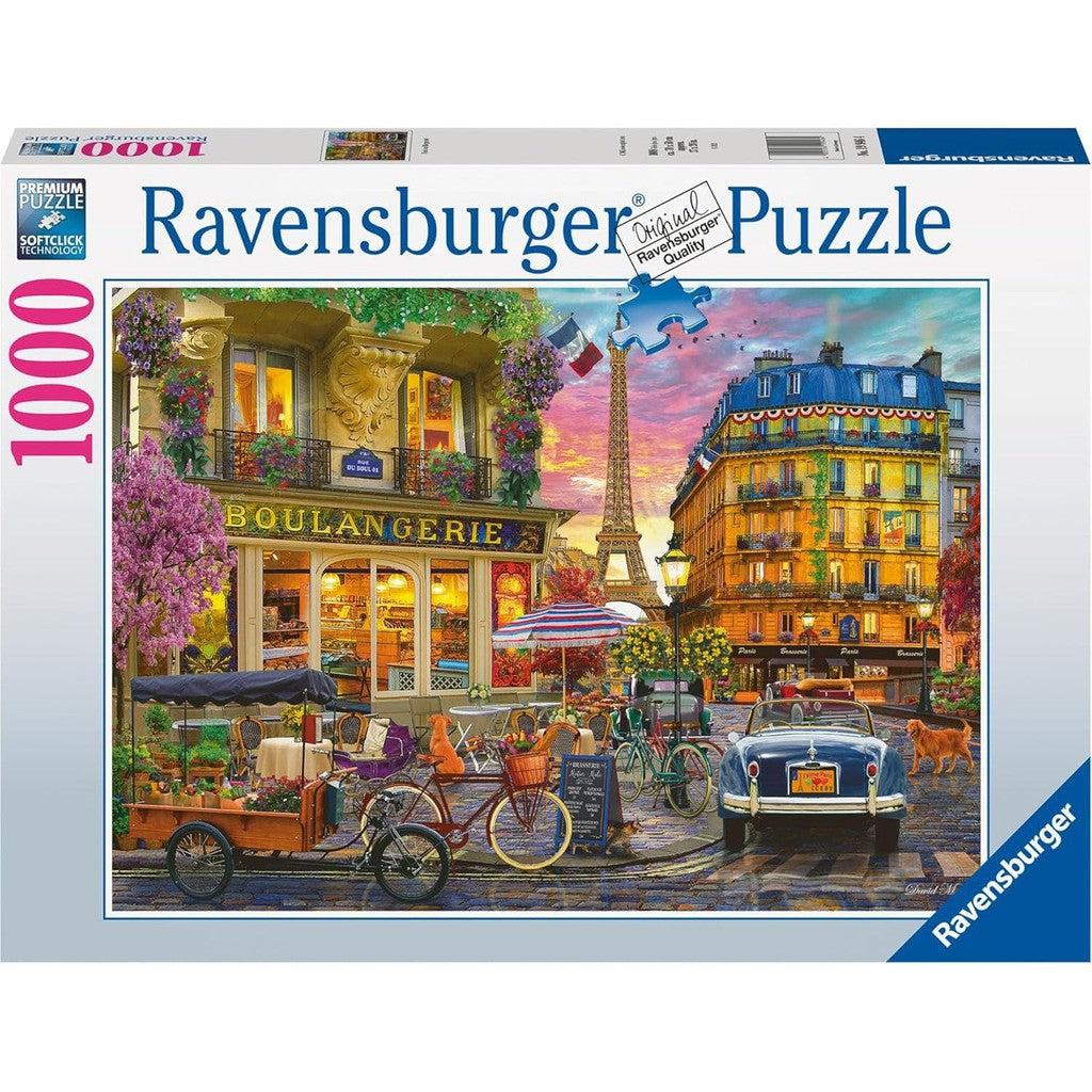 The Ravensburger 19946, a 1000-piece puzzle, captures a vibrant street scene: a charming boulangerie, bicycles waiting nearby, and a vintage car parked as dawn breaks over Paris at Sunrise. A playful dog trots along the cobblestone road, completing the picturesque tableau.