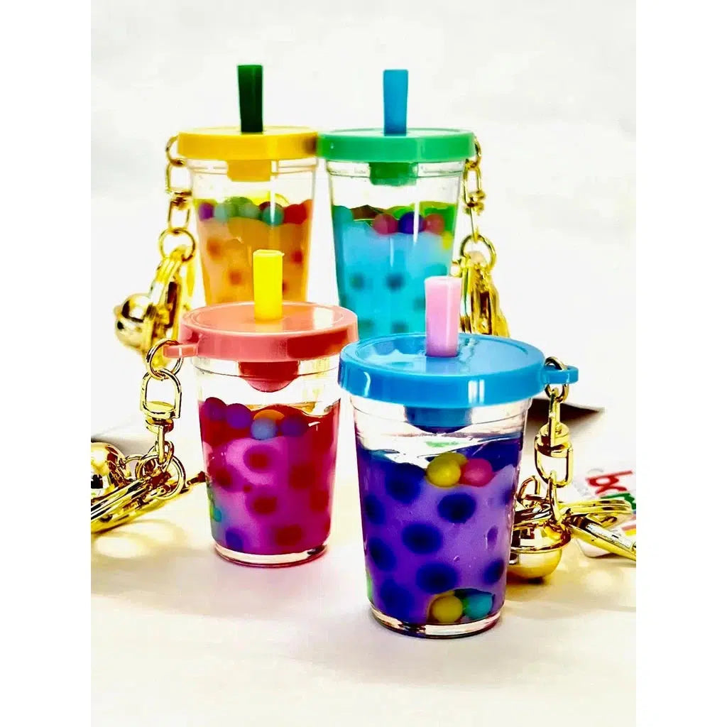 These pastel boba tea keychains feature clear cups filled with colorful beads. Each key charm has a unique colored lid and straw, adorned with gold bells––a delightful mix of fun and whimsy for your keys.