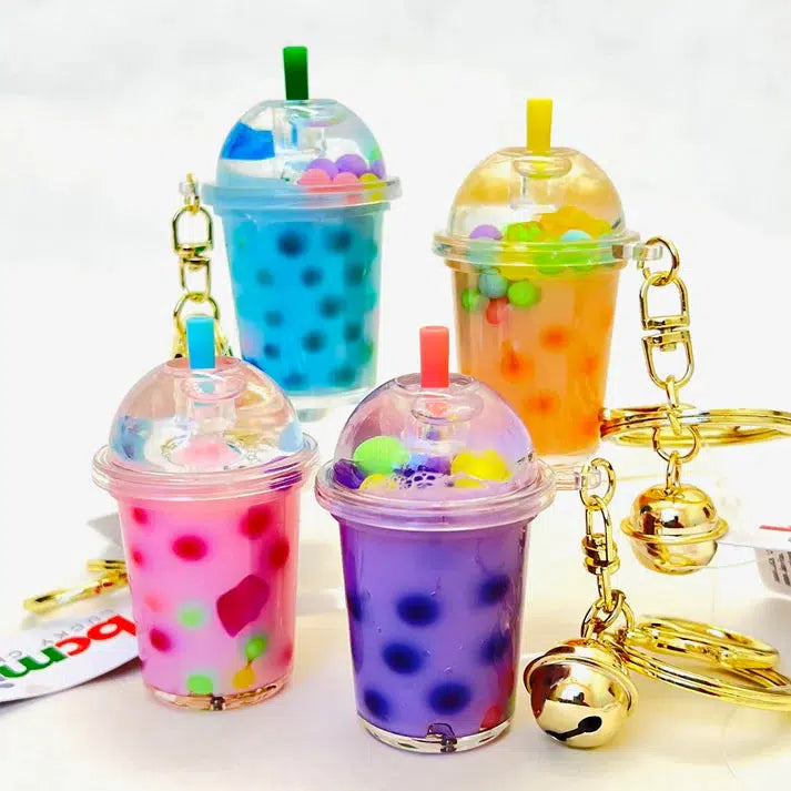 Four colorful bubble tea keychains with domed lids, each showcasing different pastel-colored beads inside. These whimsical BOBA FLOATY KEY CHARMS are attached to gold keyrings with bells, adding a touch of fun flair to your accessories.