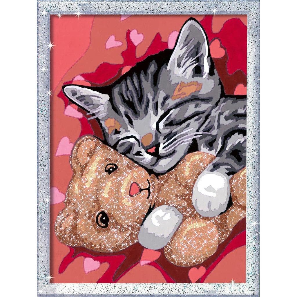 Illustration of a gray-striped kitten snuggling with a brown teddy bear on a pink heart-patterned background, reminiscent of a Ravensburger Kids Arts and Crafts project, all surrounded by a sparkly silver frame.