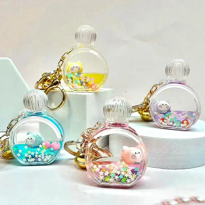 Four vibrant keychains shaped like small bottles with miniature bear figures inside, surrounded by star-shaped confetti, and offering assorted designs, are displayed on a white surface.