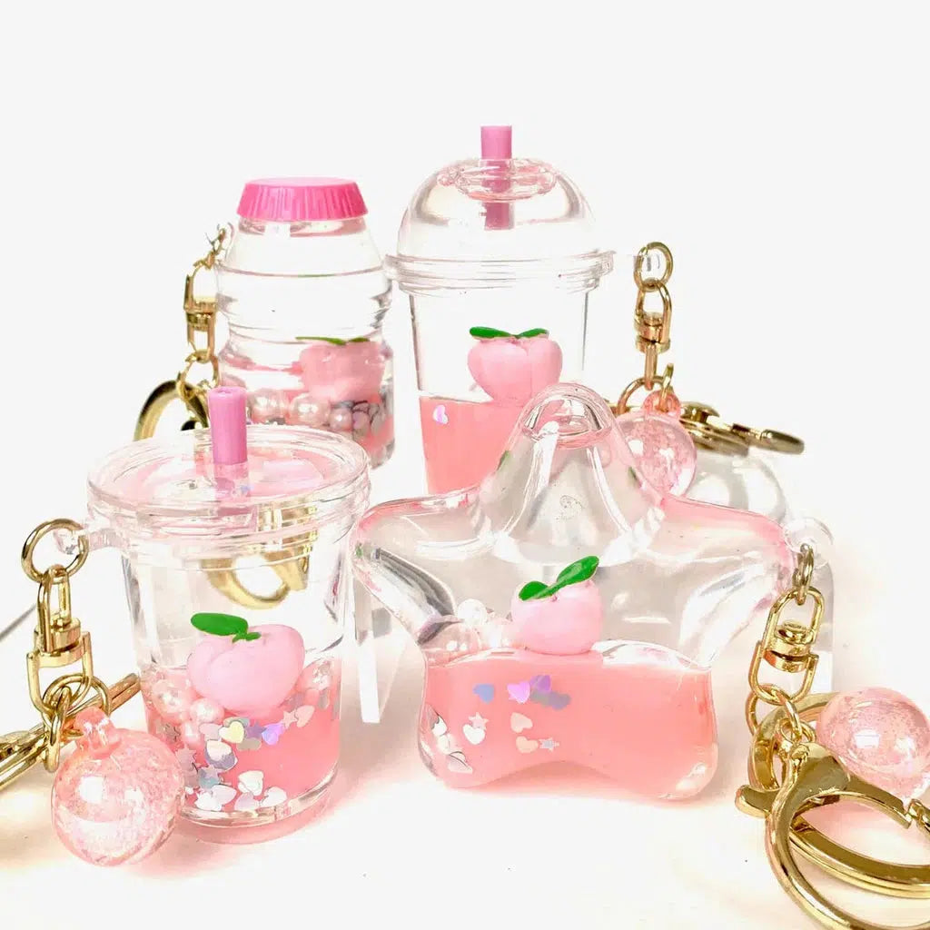 Four keychains featuring miniature pink drink cups adorned with peach designs and heart-shaped confetti, each complemented by a cute boba key charm for an extra touch of whimsy.