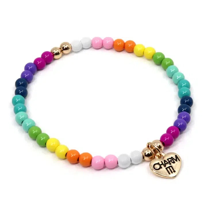 The Rainbow Stretch Bead Bracelet is a colorful, charmable piece with a gradient of hues and a gold heart charm engraved with "CHARM IT!" that will seamlessly customize her collection.