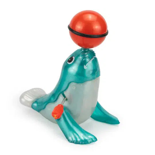 A performing seal balances a red ball on its nose, complete with a classic wind-up key on its side, reminiscent of a vintage circus toy.