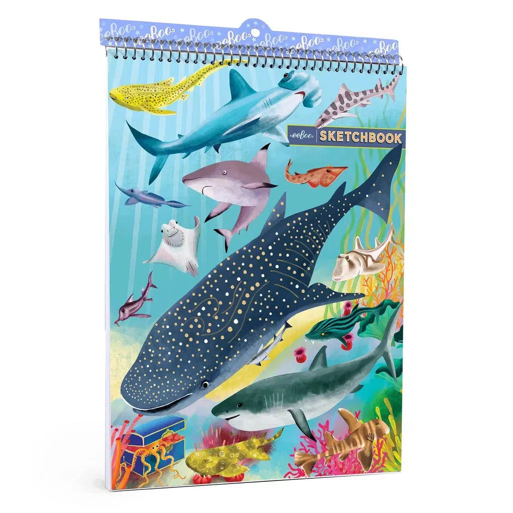 The image shows a sketchbook with spiral bindings on the top with the cover of the book showing off art of various sharks.