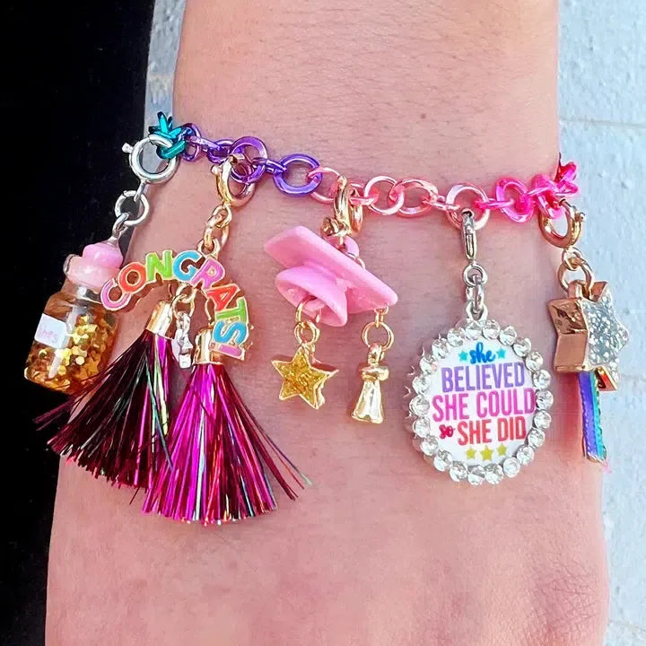 Introducing the vibrant CHARM IT! bracelet, adorned with a sparkling array of charms. It features a "Congrats!" sign, a pink star, a playful tassel, and an inspiring round charm boasting "She believed she could, so she did." Plus, don't miss the cute Polar Bear charm for an added touch of whimsy.