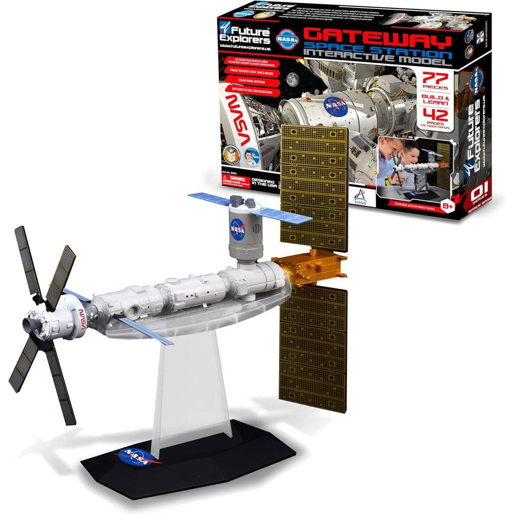 Model of a space station with rotating solar panels, displayed on a stand. The packaging in the background features MUKIKIM NASA Future Explorers and highlights its interactive space exploration and STEM education benefits.