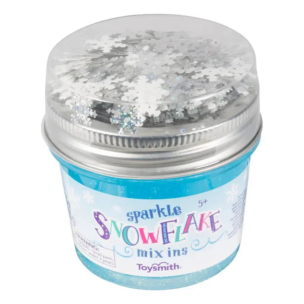 Display of ToySmith Sparkle Snowflake Mix-Ins, with 12 jars featuring shimmering snowflake designs and holographic glitter confetti in a blue and white themed packaging.