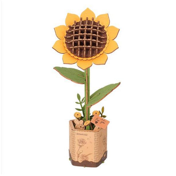 A wooden model of a bright yellow sunflower on a stem, standing in a wooden base.